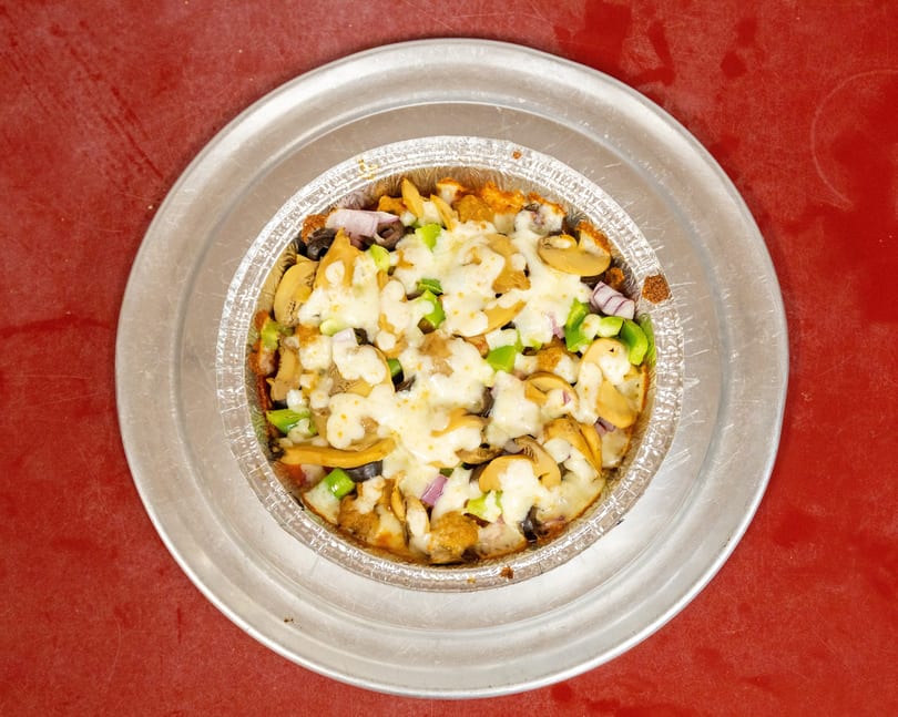 Baked dish with melted cheese, mushrooms, green peppers, red onions, and olives in a foil pan.