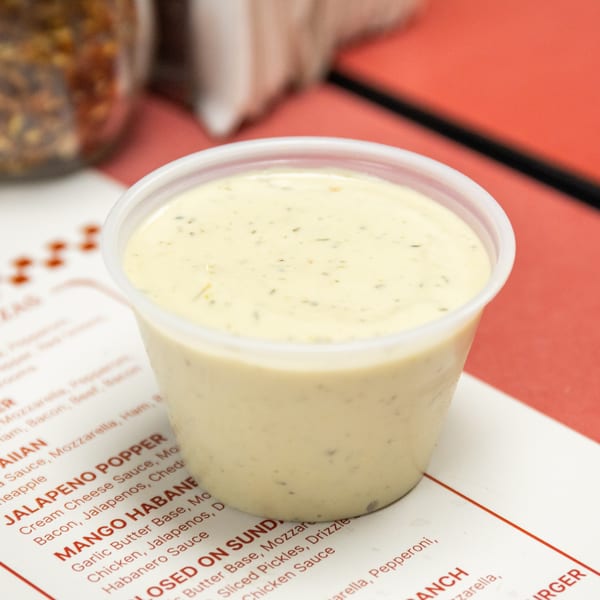 Creamy herb dressing in a plastic cup on a menu with red text.