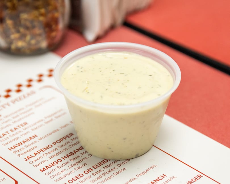Creamy herb dressing in a plastic cup on a menu with red text.