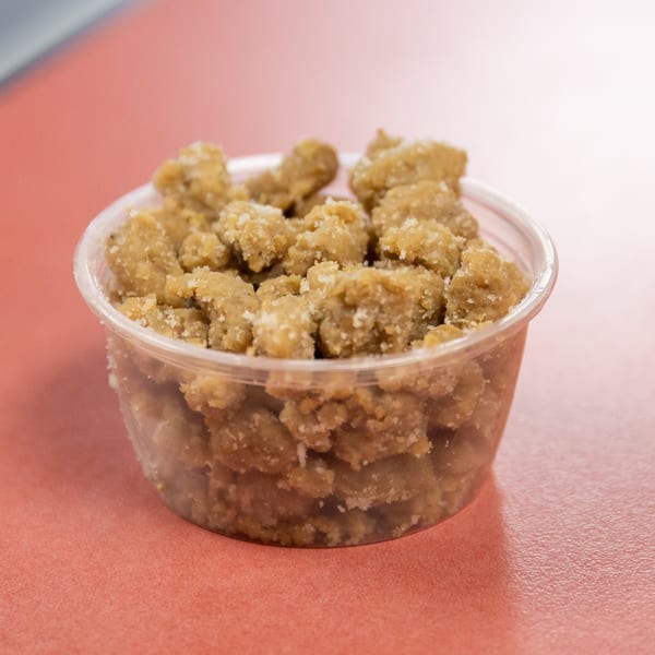 Sugary brown dessert crumbles in a clear plastic container on a reddish-orange table.