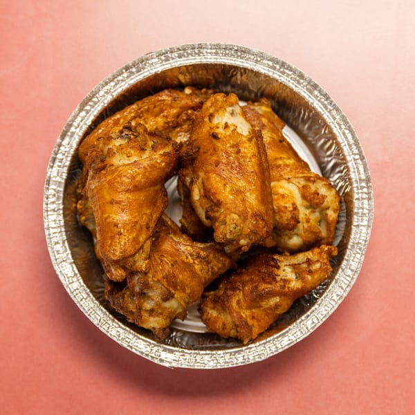 Golden-brown chicken wings in a round foil container on a pink background, viewed from above.