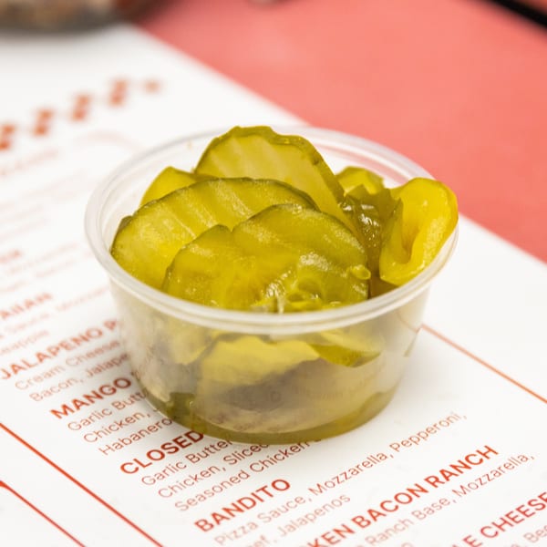 Bright green sliced pickles in a small cup sit on a restaurant menu.