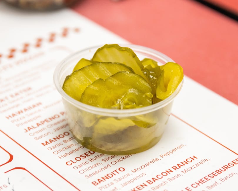 Bright green sliced pickles in a small cup sit on a restaurant menu.