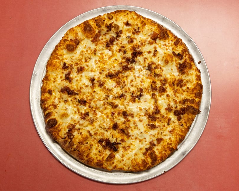 Whole round pizza with melted cheese and savory brown crumbles on a metal pan.