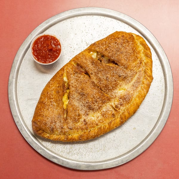 Golden brown calzone with cheese sprinkles and a side of marinara sauce on a metal pan.